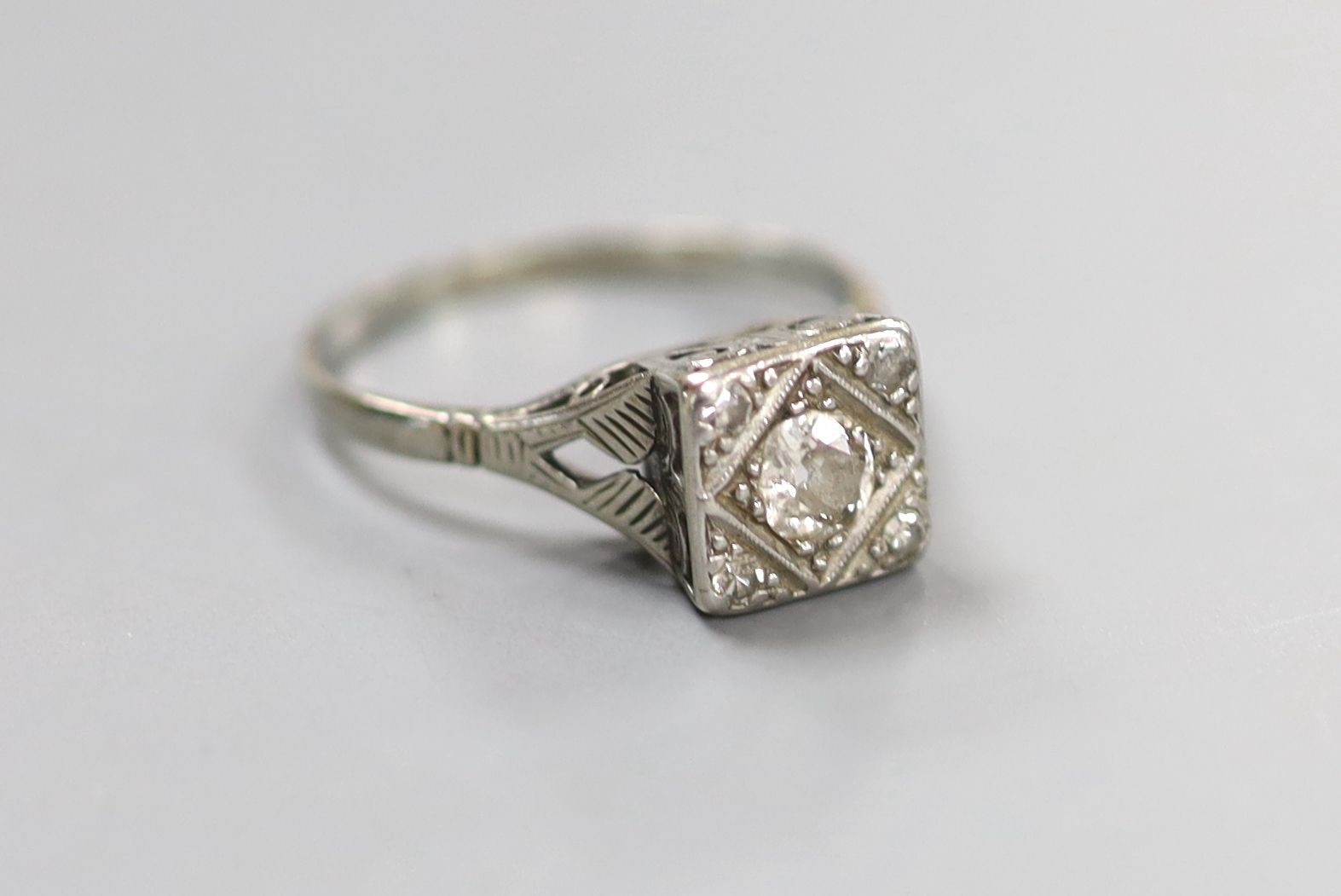A 1920's/1930's white metal and single stone round cut diamond set square ring, with diamond set corners, size O/P, gross weight 2.9 grams.